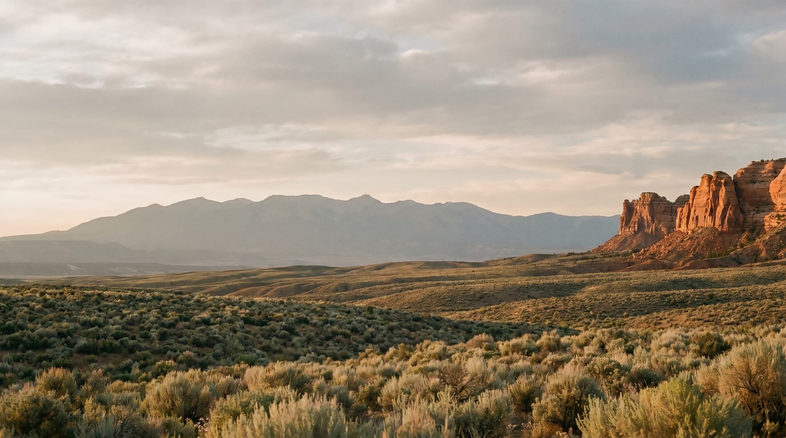 Uintah Basin landscape at golden hour — sandstone bluffs, sage plain, distant Uinta range